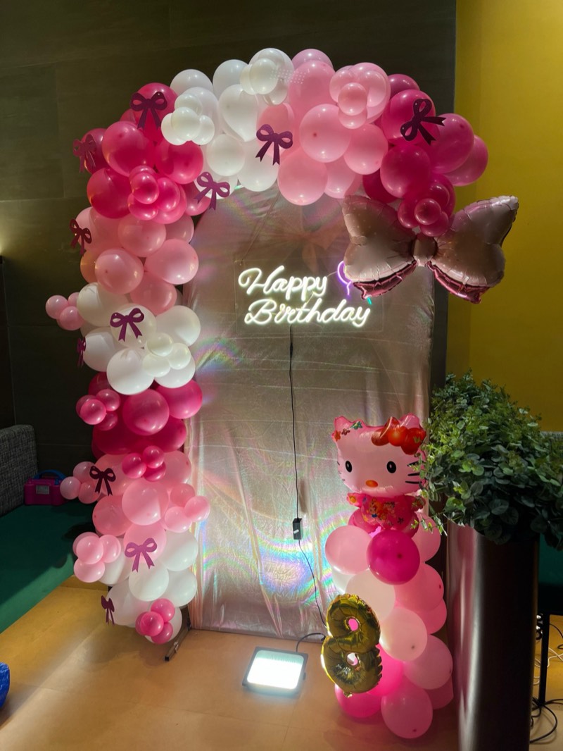 Pink and white balloon arch with bows, a character foil balloon and a neon Happy Birthday sign